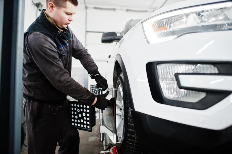 A mechanic adjusting the wheel alignment on a white car.