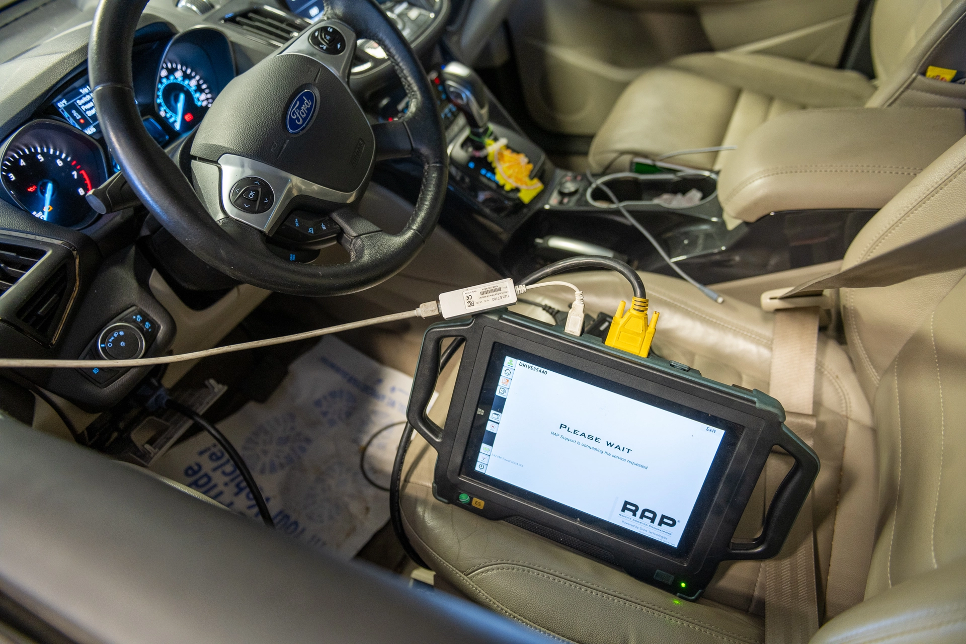 Diagnostic tablet connected to a car's dashboard for vehicle system analysis.