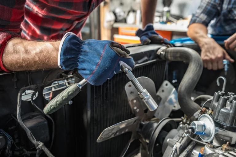 Person in a checkered shirt using a ratchet on a vehicle engine.