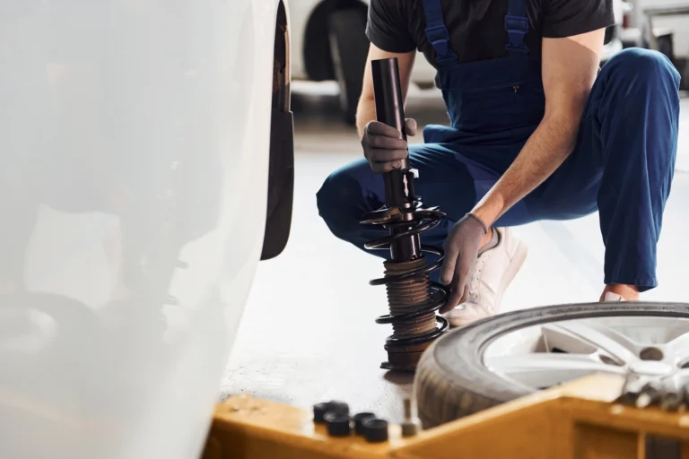 Mechanic working on car suspension near a dismounted tire.