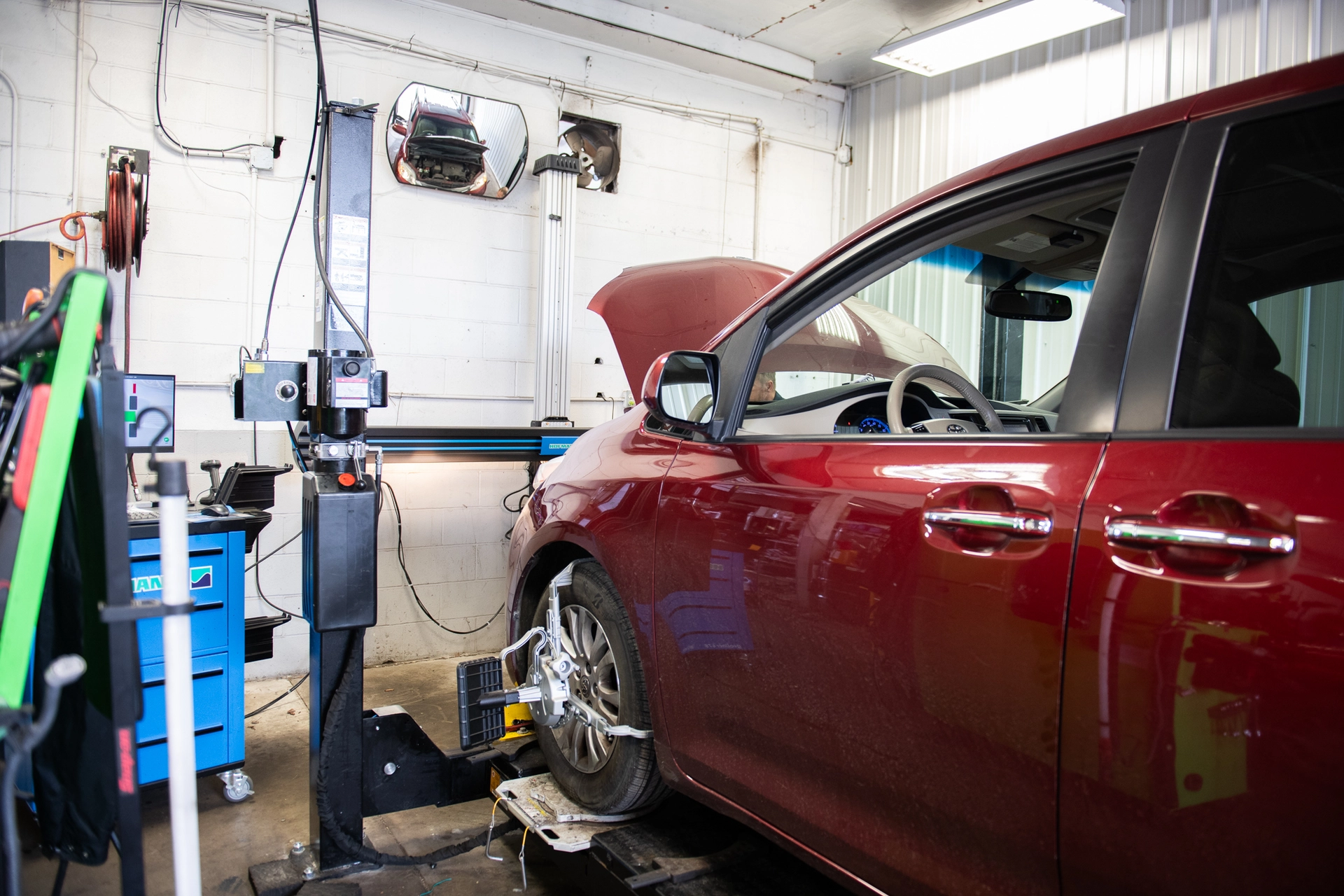 A red car undergoing a wheel alignment service in an auto repair shop.