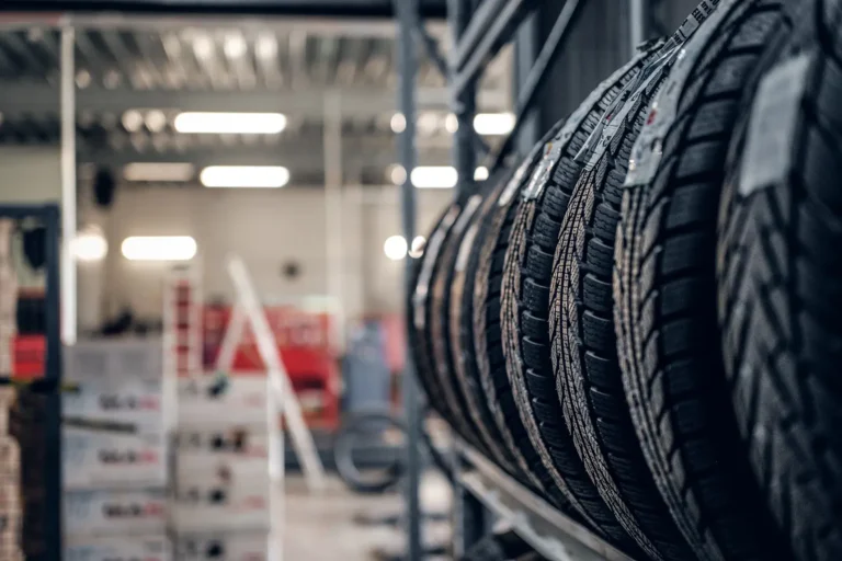 A row of various car tires displayed on a rack in an auto service garage, with a blurry background showing the workshop area.