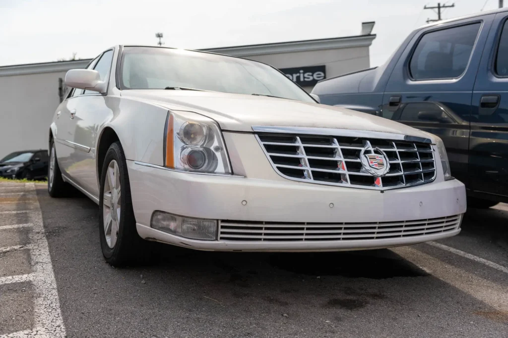 A white Cadillac sedan is parked in a parking lot next to a dark blue vehicle, with a building seen in the background.