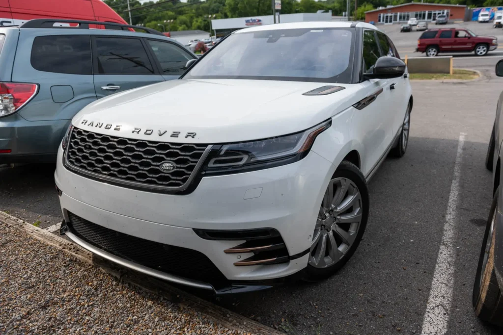 A white Range Rover Velar is parked in a lot next to other vehicles on an overcast day.