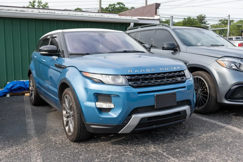 A blue Range Rover Evoque parked next to a gray SUV in a parking lot with a green building in the background.